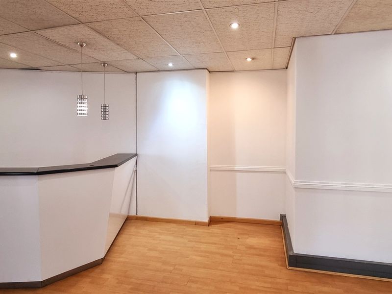 An empty office space featuring a built-in reception desk, suspended ceiling with integrated lighting, and laminate flooring.