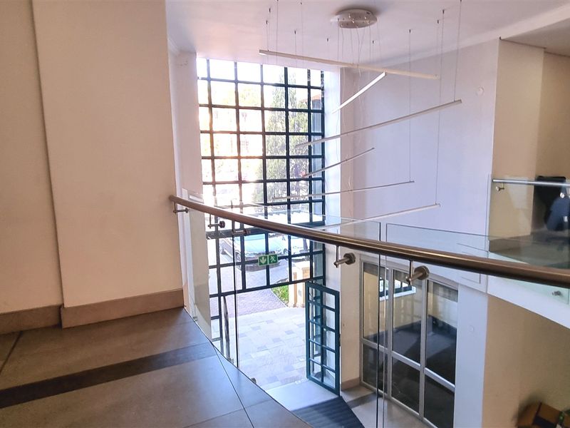 Modern office building entrance lobby featuring a double-volume space, glass balustrades, and large grid-pattern windows allowing for natural light.