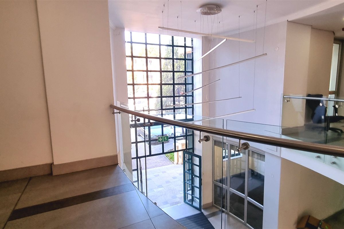 Modern office building entrance lobby featuring a double-volume space, glass balustrades, and large grid-pattern windows allowing for natural light.