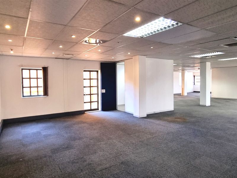 Spacious open-plan office area featuring suspended ceilings, recessed lighting, and carpeted flooring with multiple windows providing natural light.