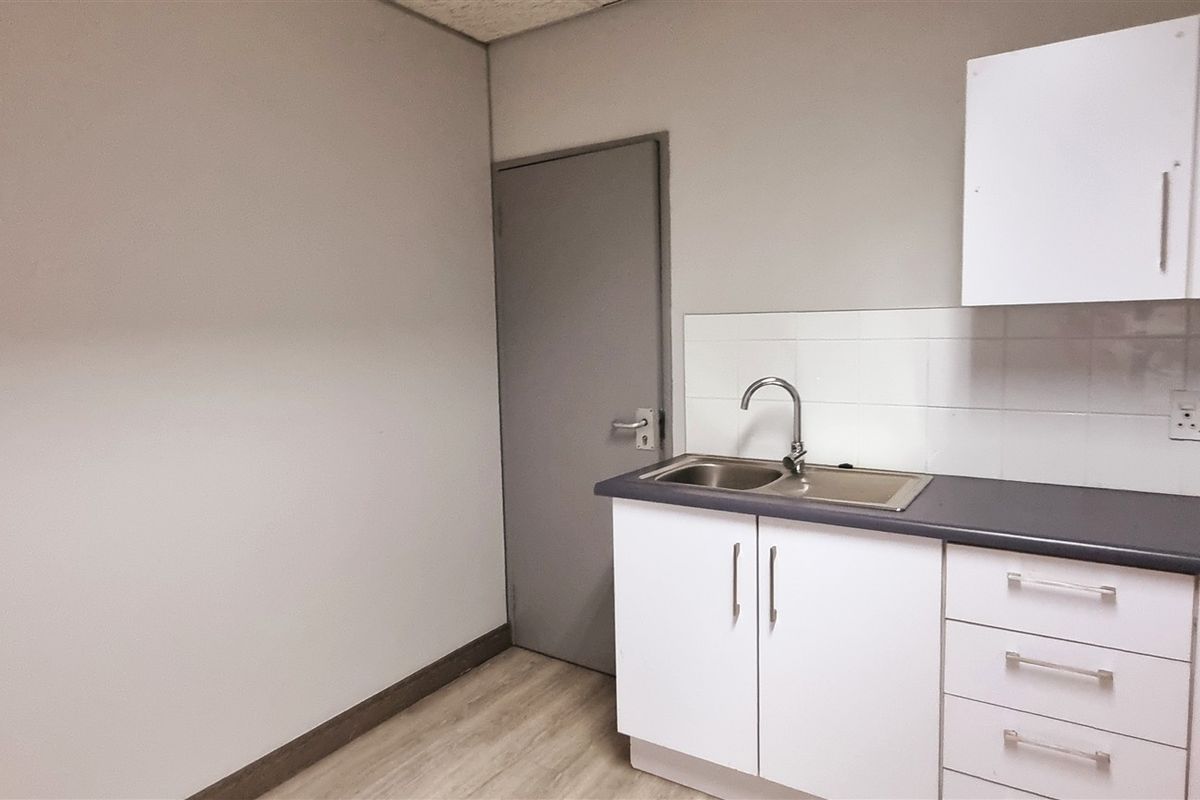 A functional office kitchenette featuring white cabinetry, a stainless steel sink, and tiled splashback, providing convenient utility space within the office environment.