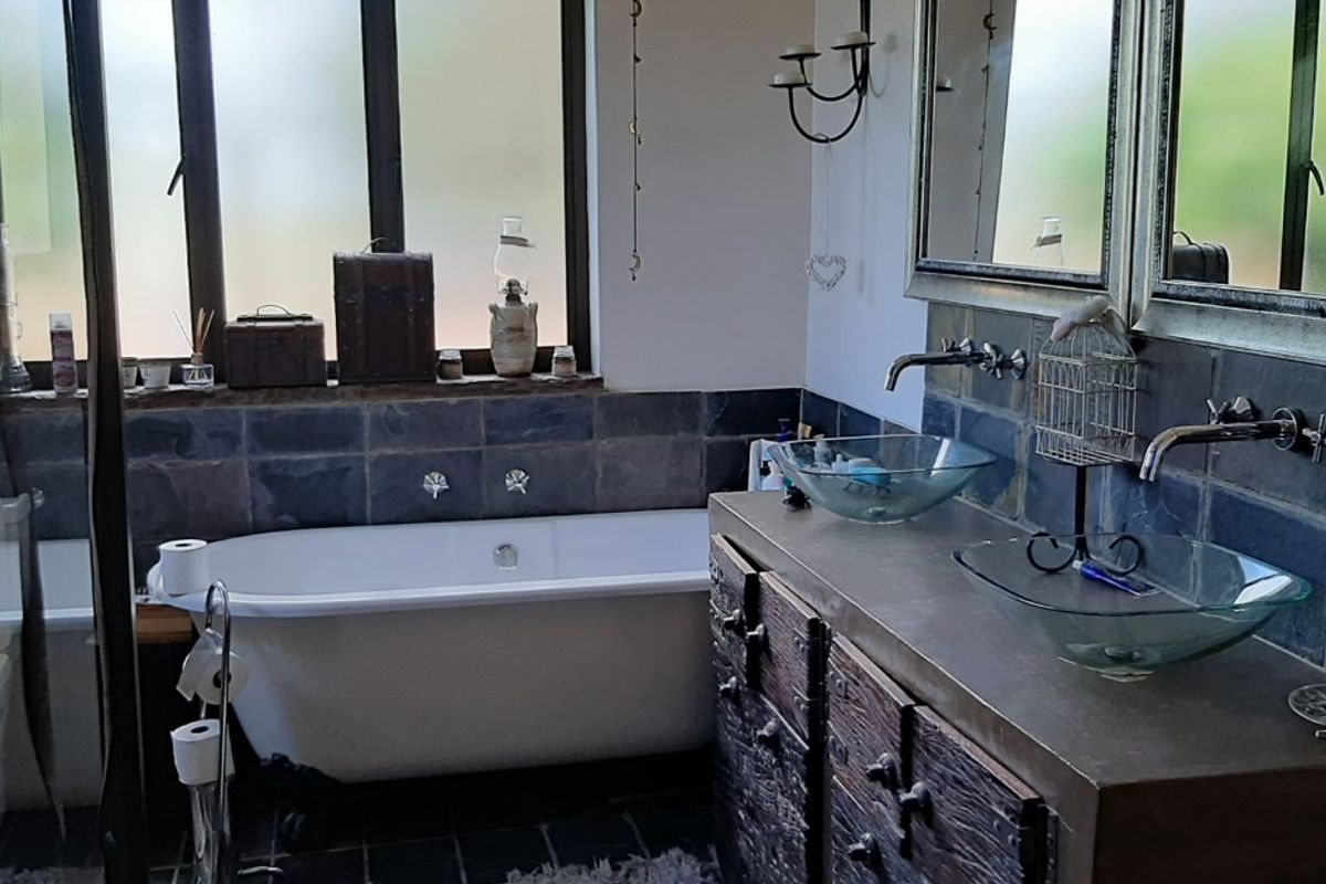 A rustic-style bathroom featuring a freestanding bathtub, double vanity with glass vessel sinks, wall-mounted faucets, and slate tile finishes.