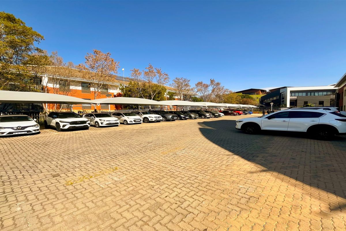 A paved outdoor parking area featuring multiple covered parking bays with shade cloth structures, serving the office building complex.