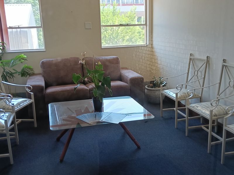 A functional office space featuring carpeted flooring, large windows providing natural light, and a wall-mounted air conditioning unit.