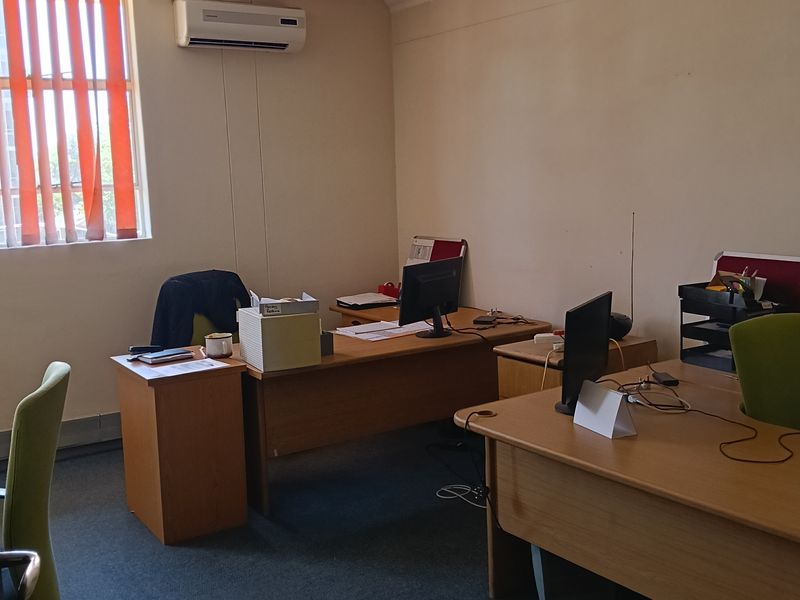 A functional office space featuring carpeted flooring, vertical window blinds, and a wall-mounted air conditioning unit.