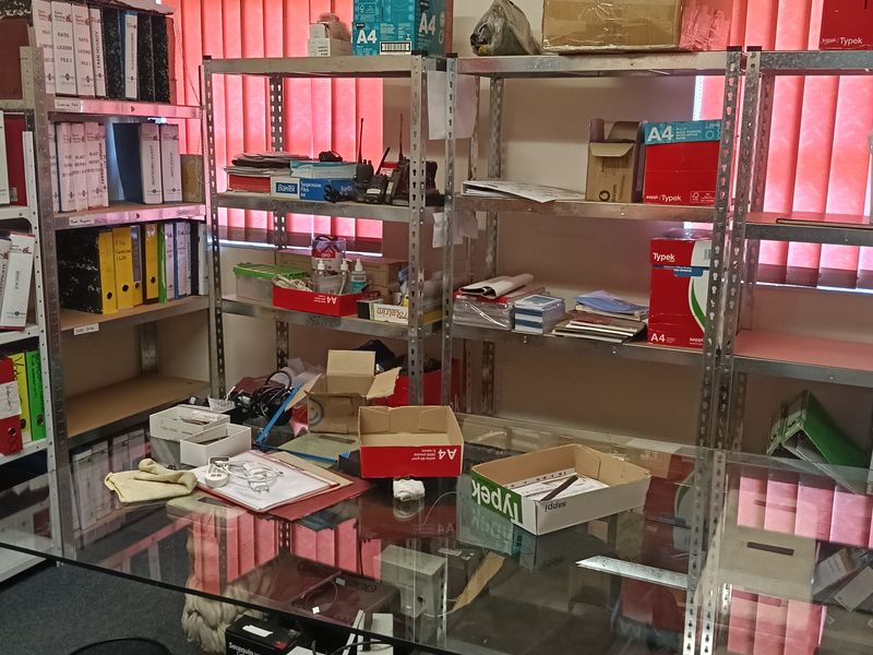 A functional office space featuring metal shelving units, vertical window blinds, and a wall-mounted air conditioning unit.