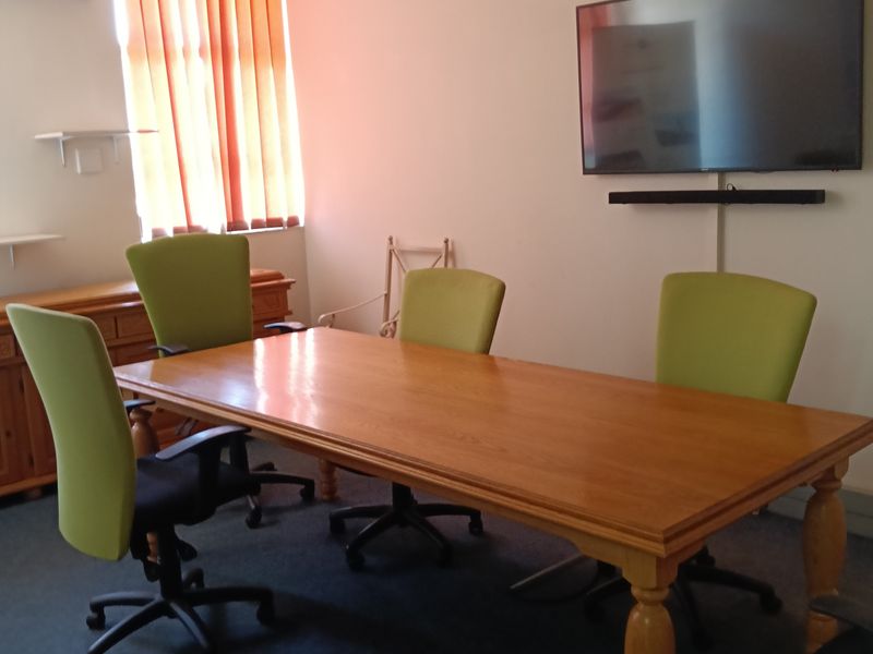 A functional office space featuring a wall-mounted television, air conditioning unit, and vertical window blinds.