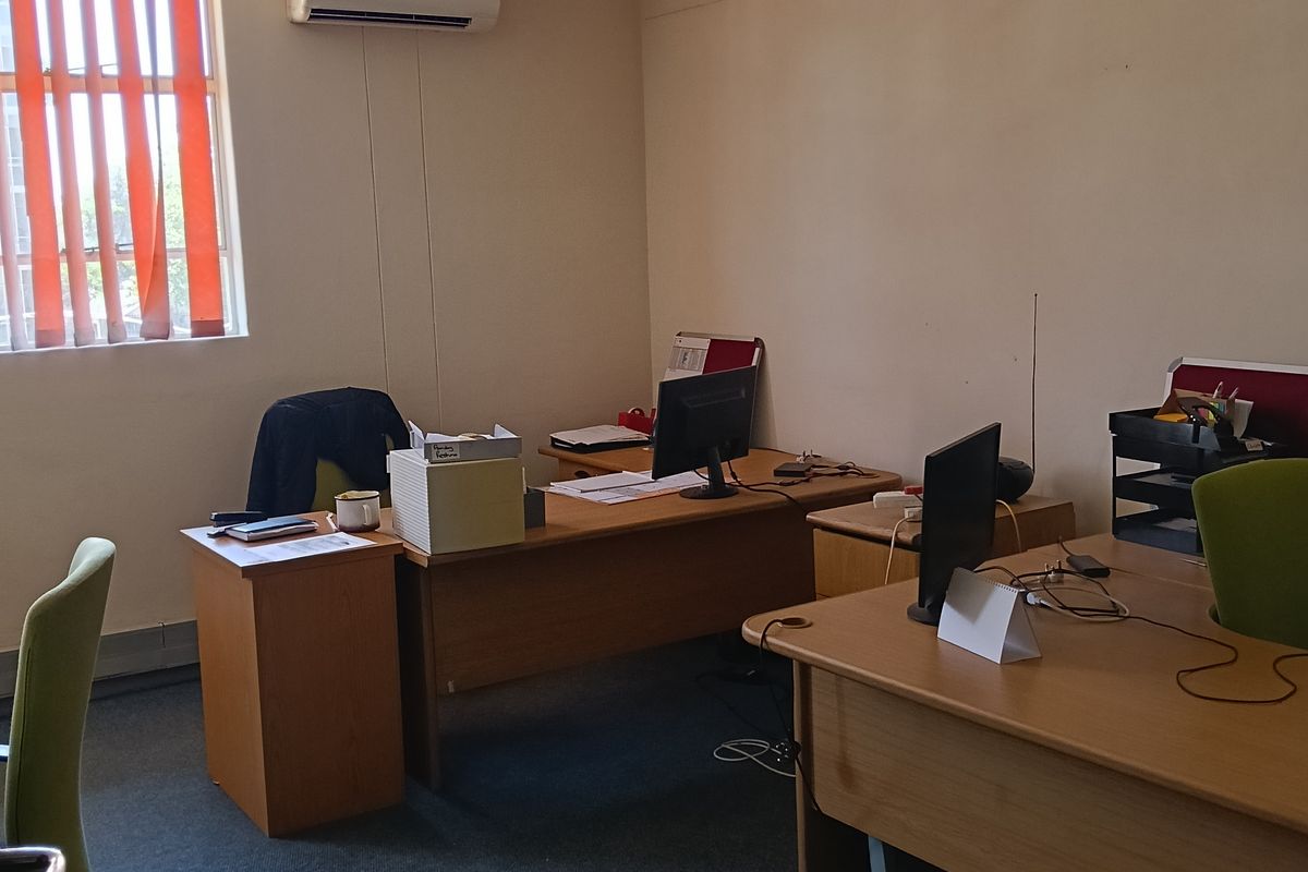 A functional office space featuring carpeted flooring, vertical window blinds, and a wall-mounted air conditioning unit.
