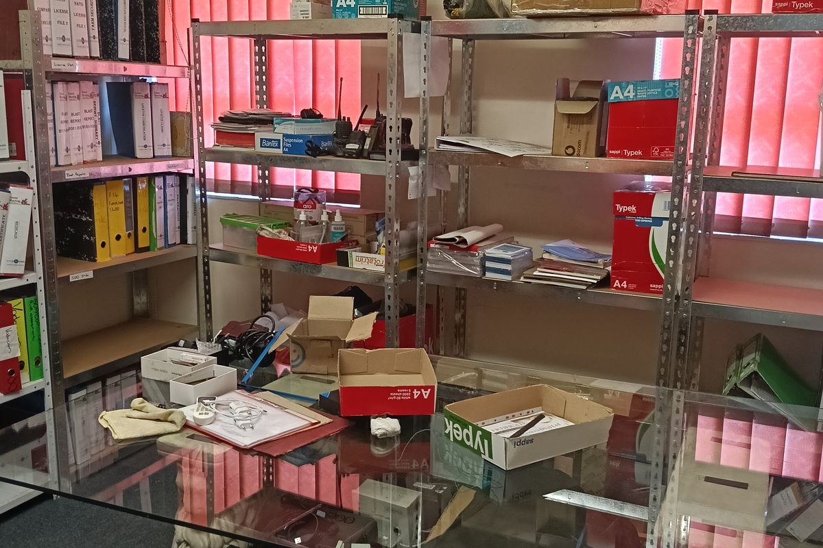 A functional office space featuring metal shelving units, vertical window blinds, and a wall-mounted air conditioning unit.