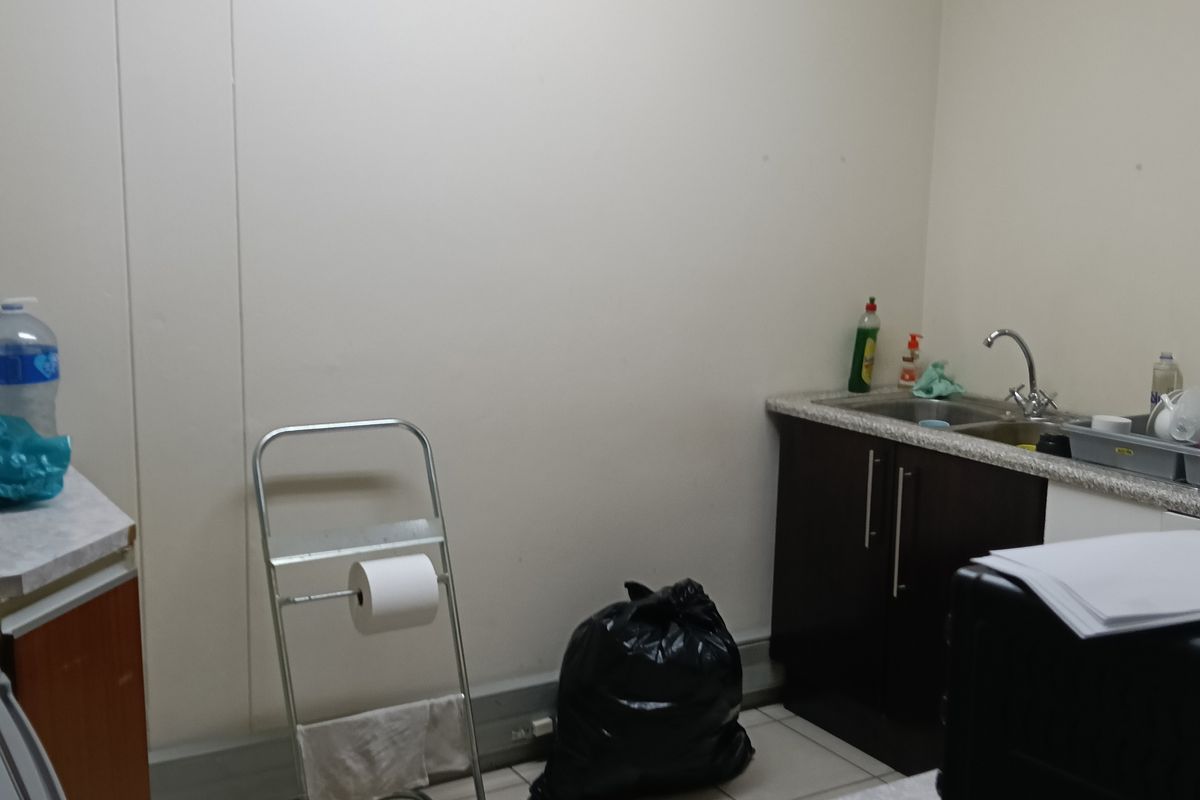 A functional office kitchenette featuring tiled flooring, laminate countertops, base cabinetry, and a wall-mounted air conditioning unit.