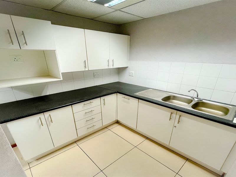 A clean and functional office kitchenette featuring white cabinetry, dark laminate countertops, a double stainless steel sink, and tiled flooring.