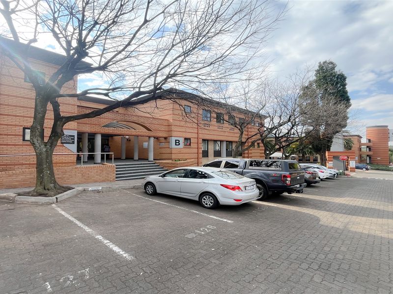 Front exterior view of a multi-story brick office building featuring a paved parking area and a covered main entrance.