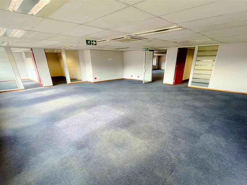 A spacious, vacant open-plan office area featuring suspended ceilings, recessed lighting, and glass partition doors, ready for custom fit-out.