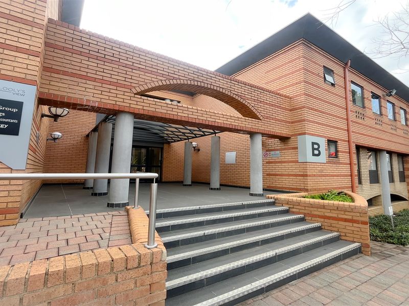 Front entrance of office building B, featuring a brick facade, concrete columns, and a tiled staircase with metal handrails.