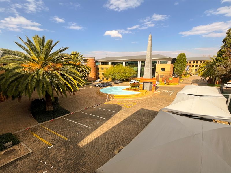Elevated view of an office park courtyard featuring paved parking, shade structures, a central water feature, and landscaped grounds.