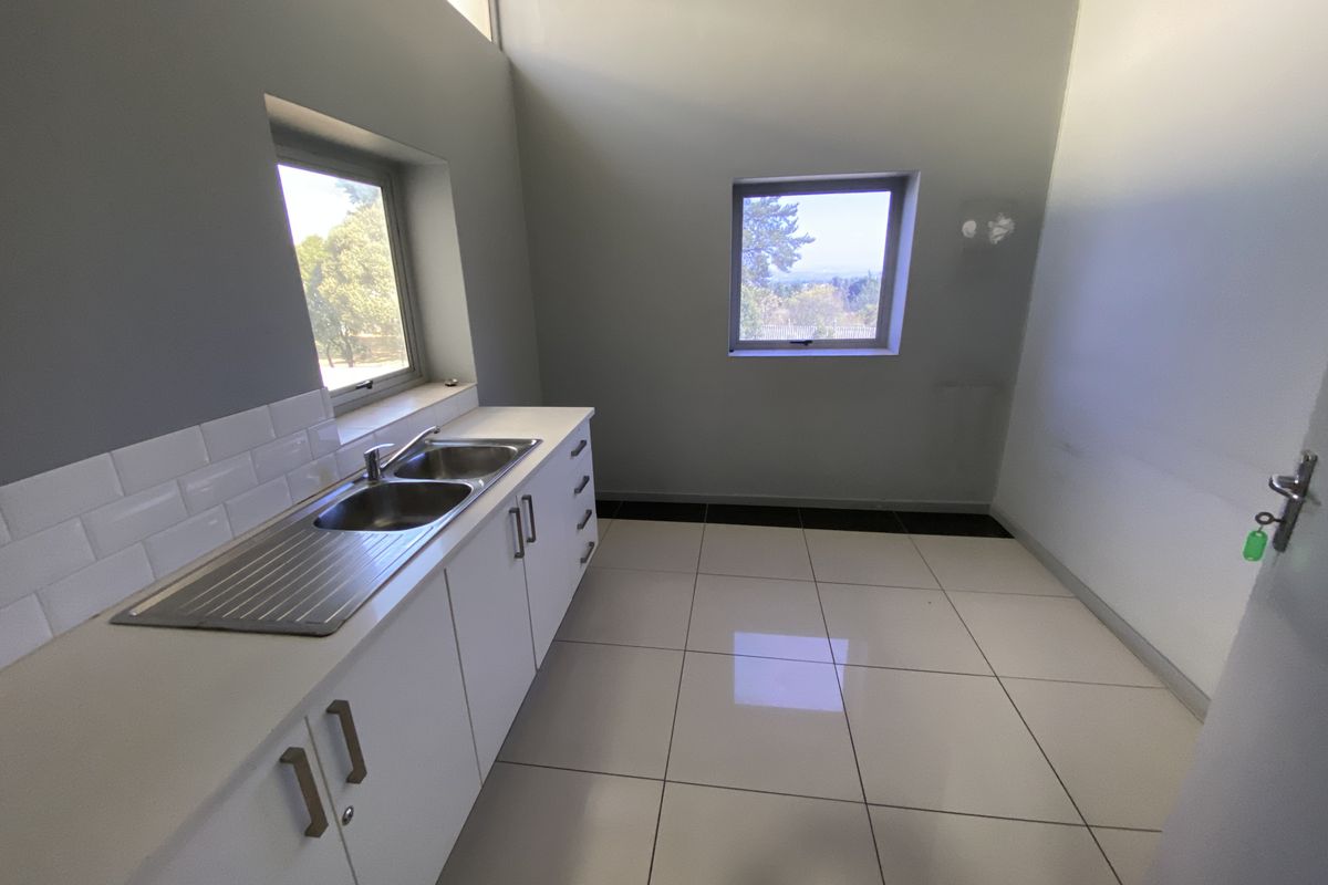 A clean, functional kitchenette featuring white cabinetry, a stainless steel double sink, subway tile backsplash, and polished floor tiles.