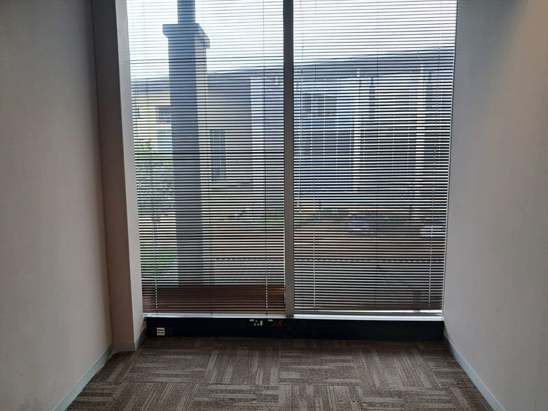A vacant office space featuring floor-to-ceiling windows with venetian blinds, carpeted flooring, and integrated electrical trunking along the base of the window.