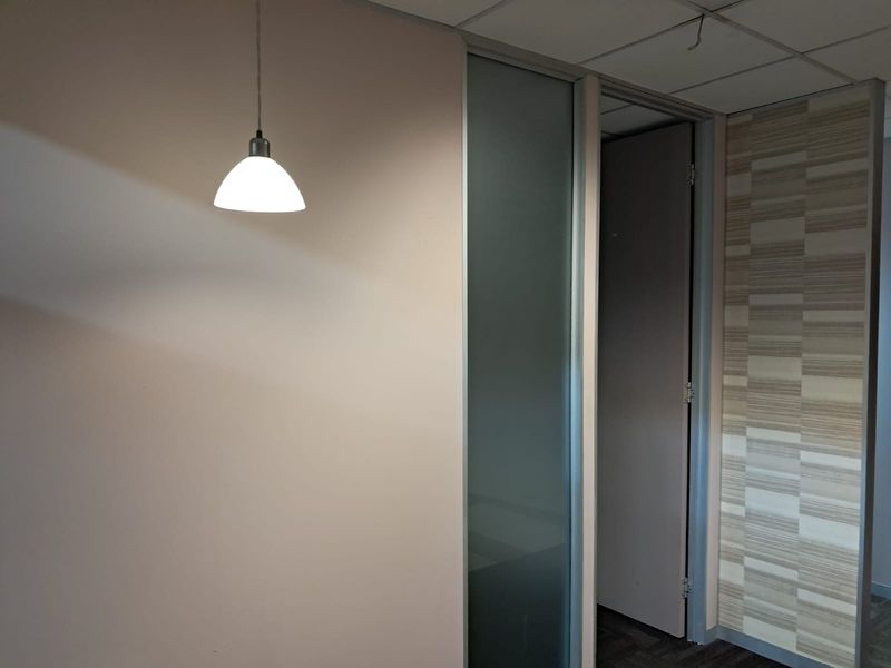 A vacant office space featuring a frosted glass partition, textured accent wall, and suspended ceiling with a pendant light fixture.