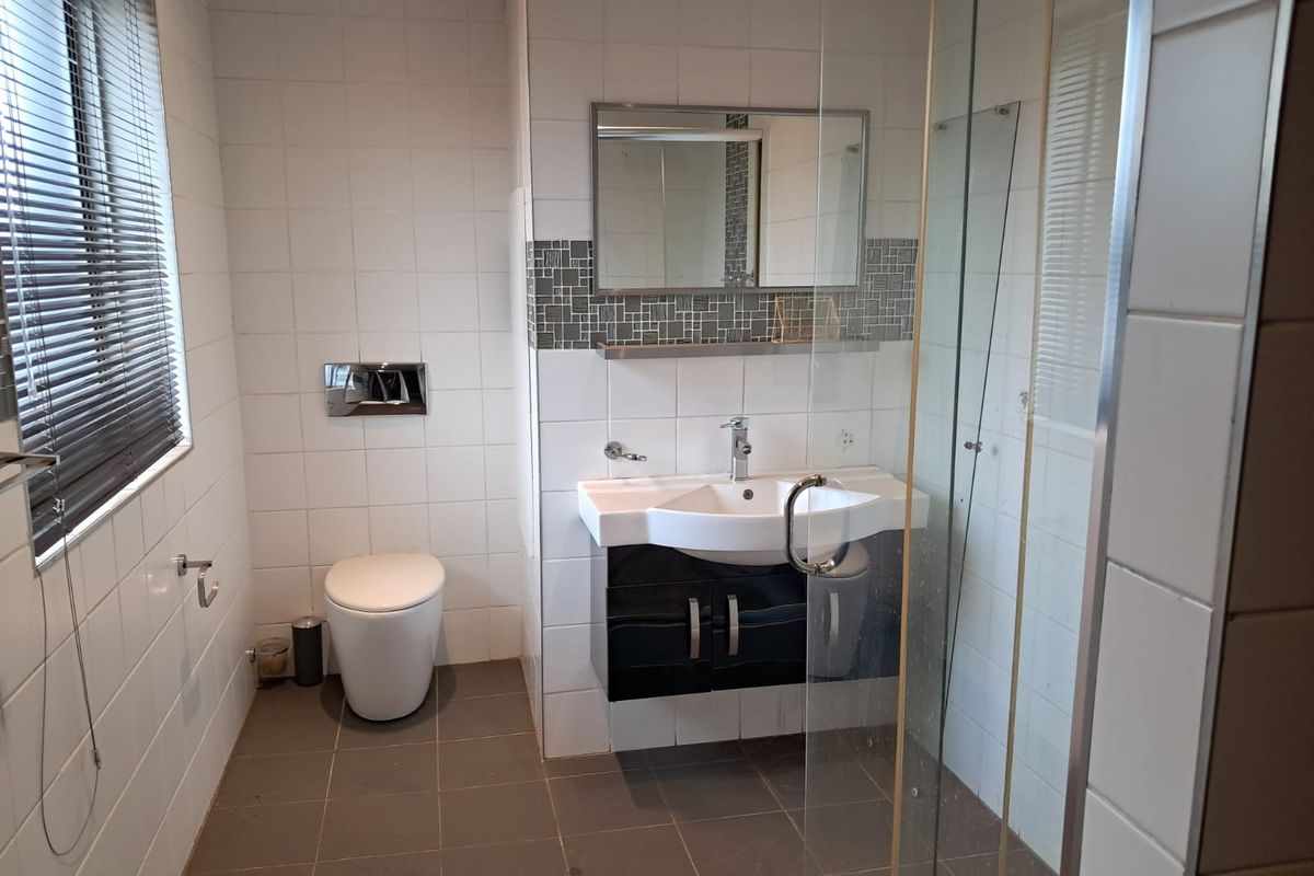 A clean, modern bathroom featuring a wall-mounted toilet, vanity basin, and a glass-enclosed shower with neutral tiled finishes.