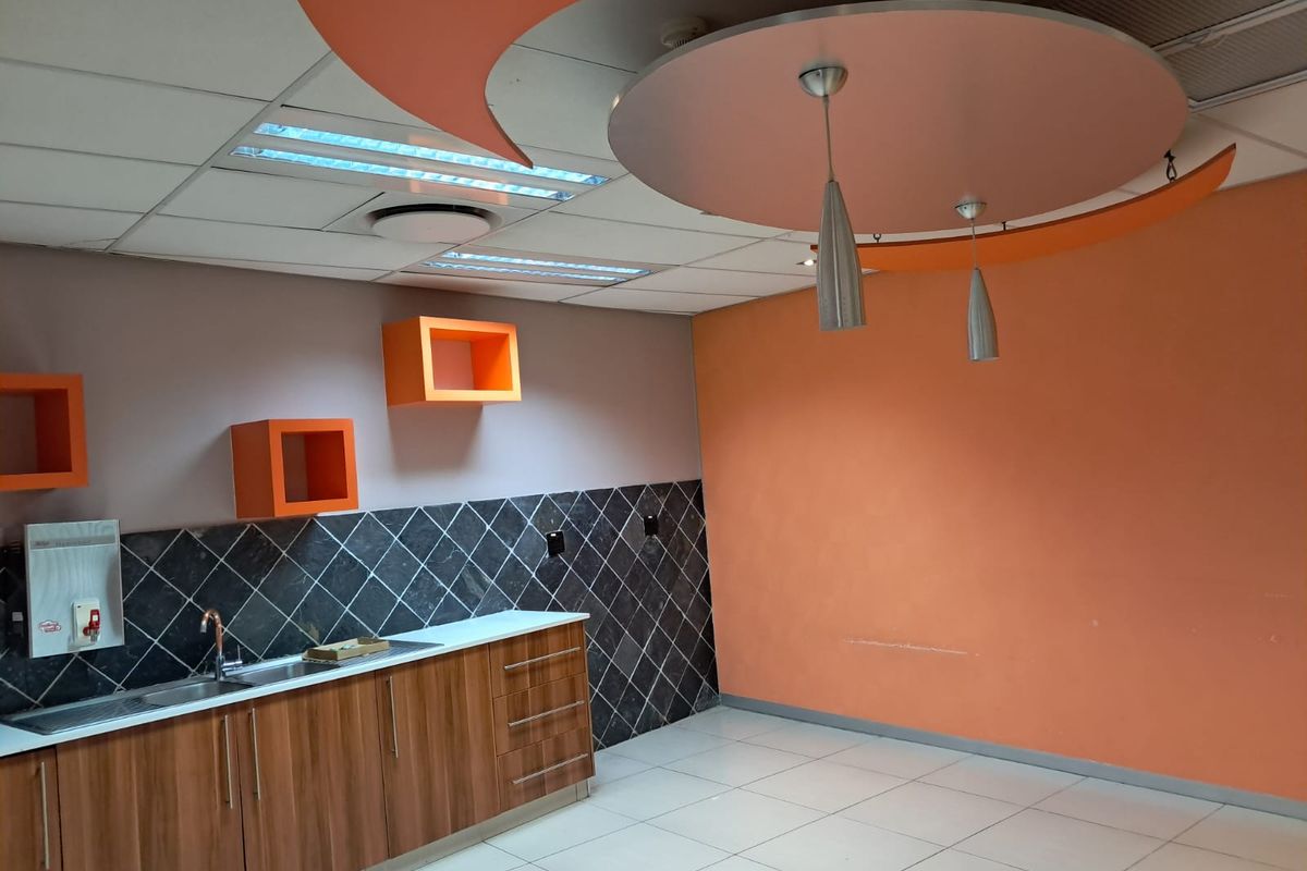 A functional office kitchenette featuring built-in cabinetry, a stainless steel sink, tiled backsplash, and decorative suspended ceiling elements.