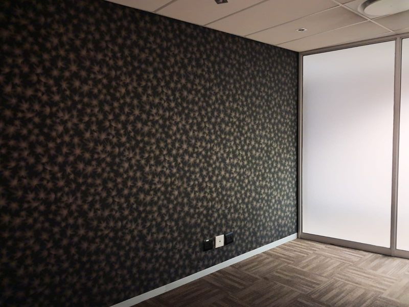 A modern, empty office space featuring patterned wallpaper, carpeted flooring, and a frosted glass partition wall.