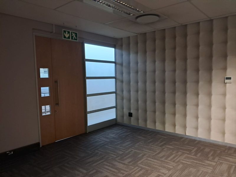 Empty office space featuring acoustic wall paneling, carpet tiles, a suspended ceiling with recessed lighting, and a modern timber entrance door with frosted glass sidelight.