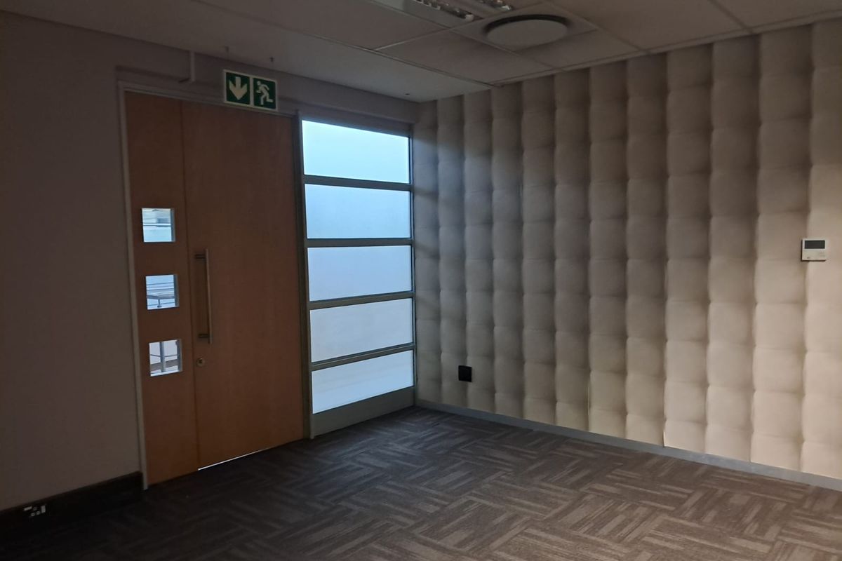 Empty office space featuring acoustic wall paneling, carpet tiles, a suspended ceiling with recessed lighting, and a modern timber entrance door with frosted glass sidelight.