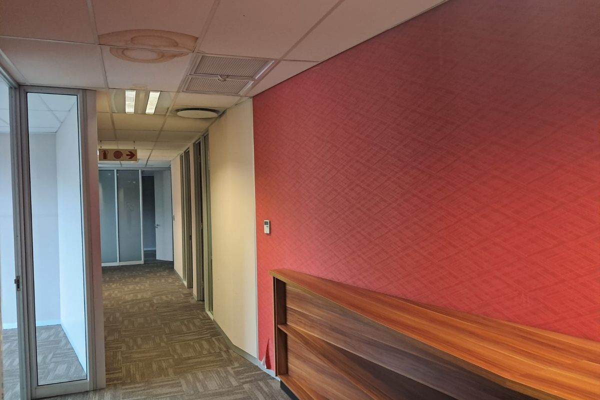 A professional office hallway featuring glass partitions, carpeted flooring, a built-in wooden shelving unit, and a distinctive red accent wall.