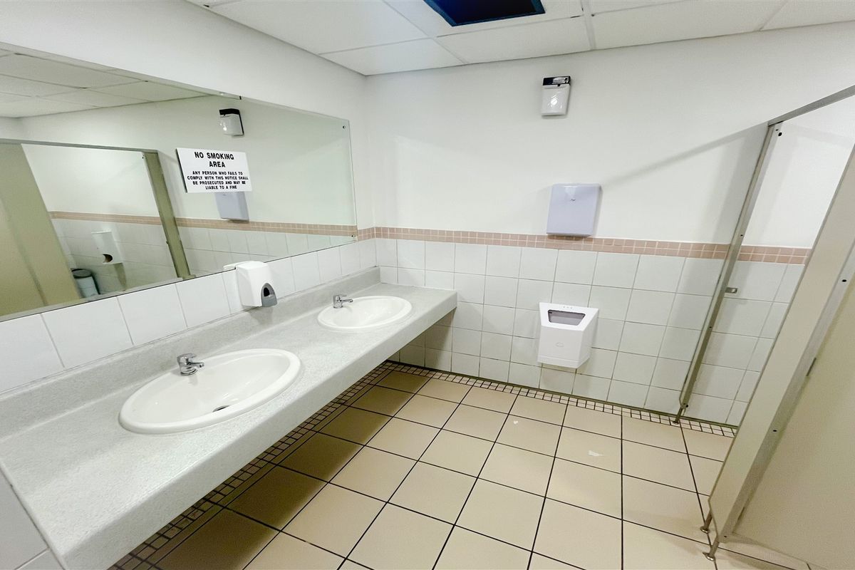 A functional office restroom featuring dual vanity basins, tiled flooring, and wall-mounted sanitary fixtures.