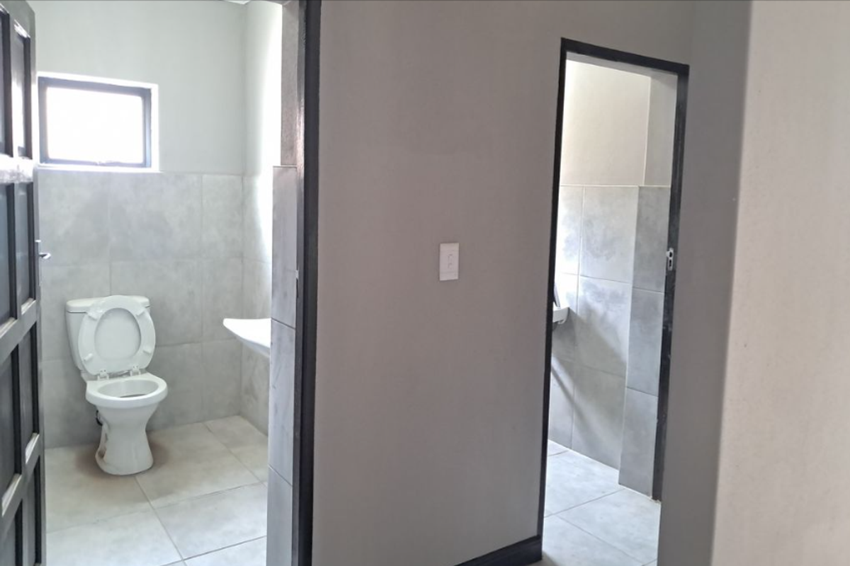 A functional bathroom space featuring tiled walls and flooring, a standard toilet, and a wall-mounted basin.