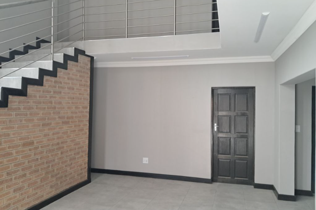 Interior view of an industrial-style space featuring a staircase with a brick accent wall, stainless steel railing, and tiled flooring.