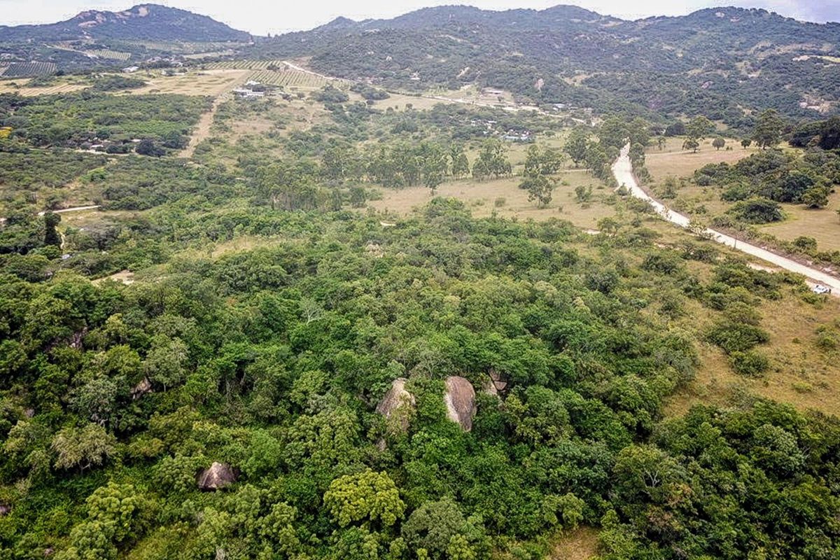 An aerial view of the expansive small holding property featuring natural indigenous vegetation, large rock formations, and a dirt access road through the landscape.