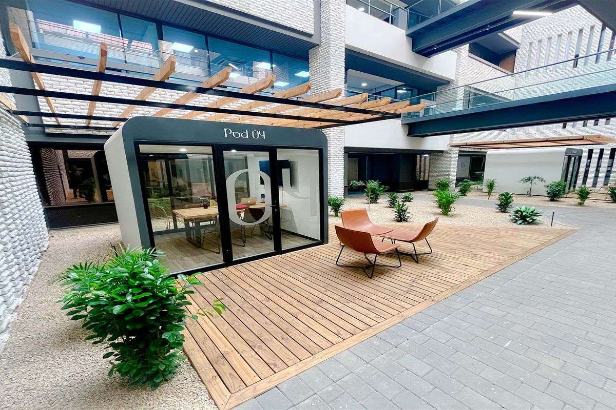 Modern office courtyard featuring a wooden deck, a glass-enclosed meeting pod, and contemporary architectural design with integrated walkways.