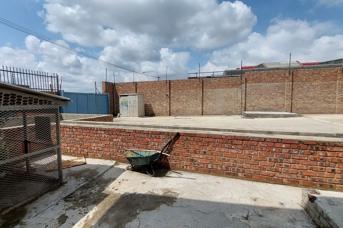 A spacious industrial rear yard featuring concrete paving, high brick boundary walls with electric fencing, and a secure utility enclosure.