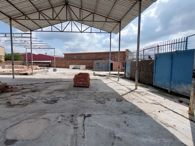 Large industrial yard featuring a covered steel structure, expansive concrete flooring, and perimeter security fencing, suitable for storage or light industrial operations.