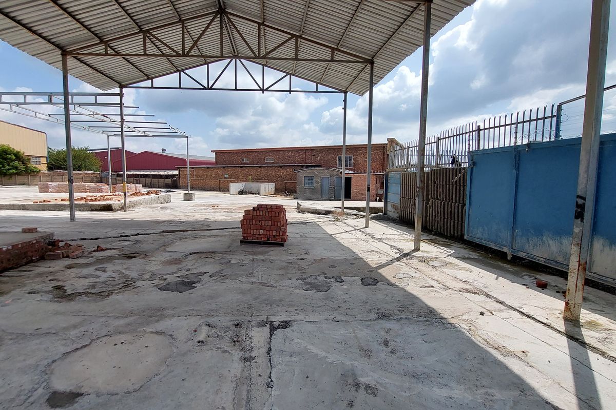 Large industrial yard featuring a covered steel structure, expansive concrete flooring, and perimeter security fencing, suitable for storage or light industrial operations.