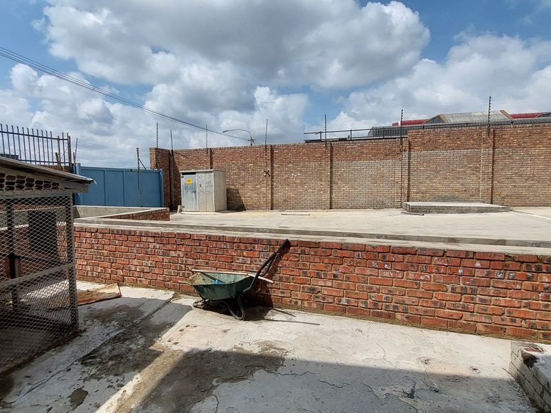 A spacious industrial rear yard featuring concrete paving, high brick boundary walls with electric fencing, and a secure utility enclosure.