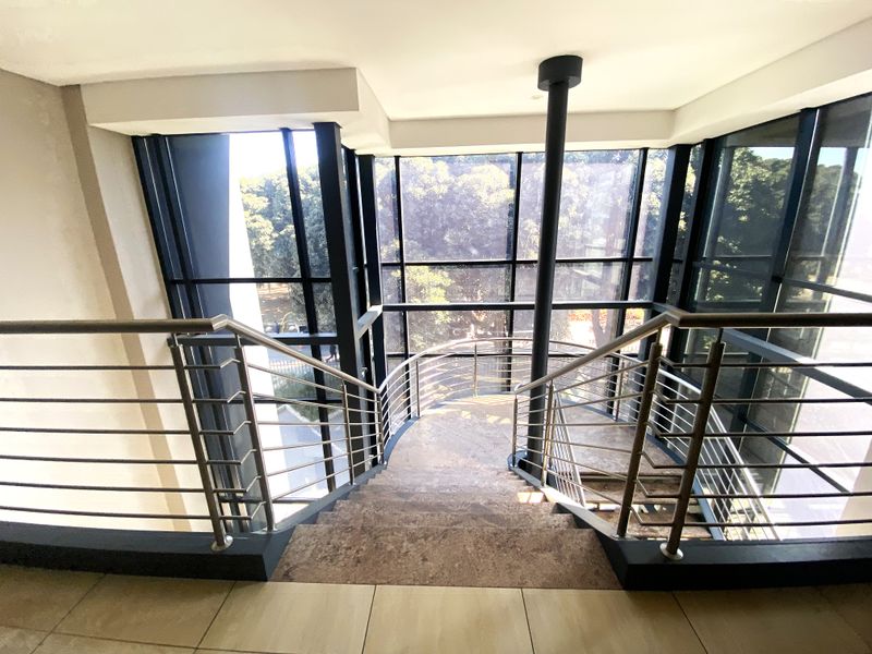 Modern office staircase featuring a stainless steel balustrade and expansive floor-to-ceiling glass windows providing ample natural light and exterior views.