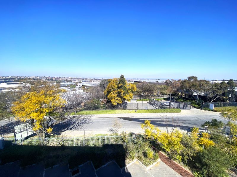 An elevated exterior view overlooking the surrounding office park area, featuring mature trees, paved access roads, and secure perimeter fencing.