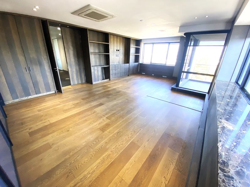 A spacious, modern office featuring high-quality hardwood flooring, extensive built-in cabinetry, recessed lighting, and a sleek marble-topped counter with large windows.