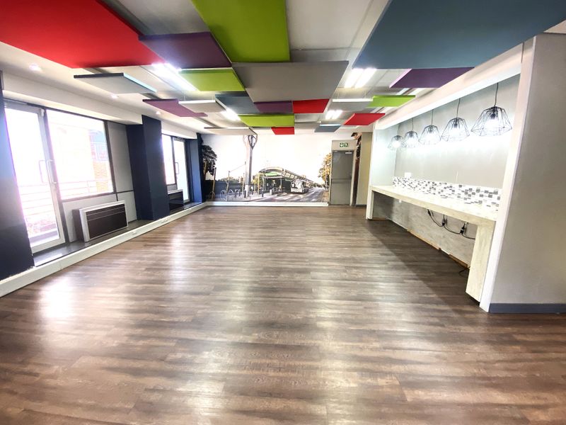 Spacious open-plan office area featuring acoustic ceiling panels, wood-look laminate flooring, a built-in service counter, and large sliding glass doors for natural light.