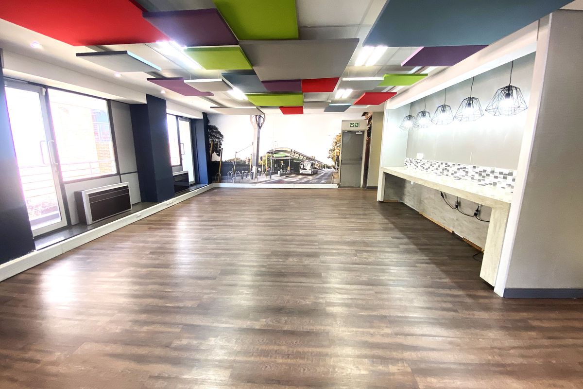 Spacious open-plan office area featuring acoustic ceiling panels, wood-look laminate flooring, a built-in service counter, and large sliding glass doors for natural light.