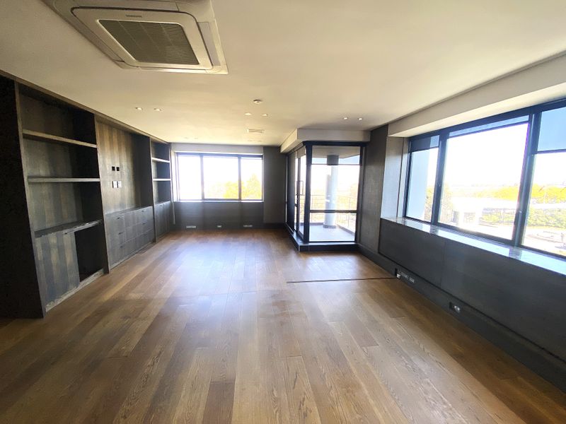 Spacious office area featuring high-quality hardwood flooring, extensive built-in cabinetry, recessed lighting, and large windows providing ample natural light and balcony access.