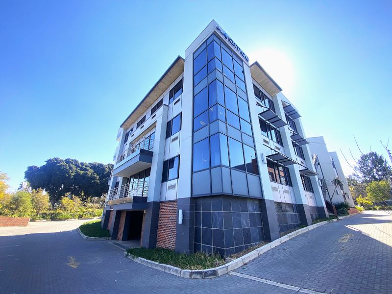 Modern multi-story office building featuring a prominent glass corner facade, brick detailing, and integrated balconies with metal railings.