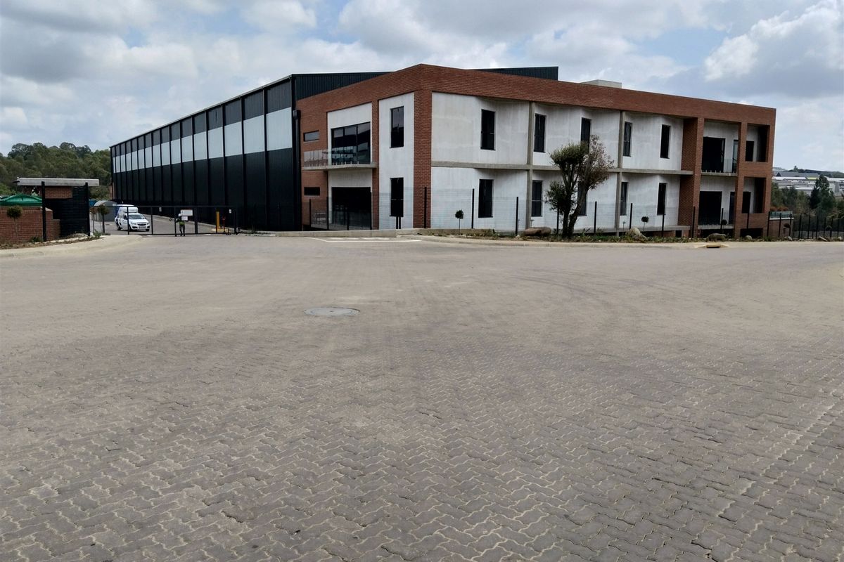 Modern industrial facility featuring a combination of brick and concrete construction with extensive metal cladding and a large paved forecourt area.