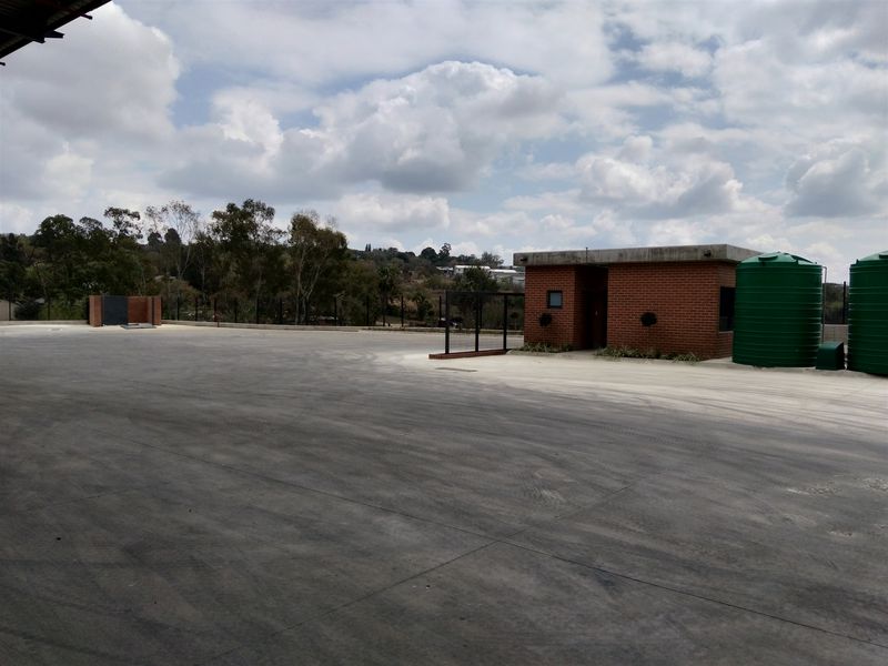 Spacious industrial yard featuring a brick guardhouse, large water storage tanks, and secure perimeter fencing on a paved concrete surface.