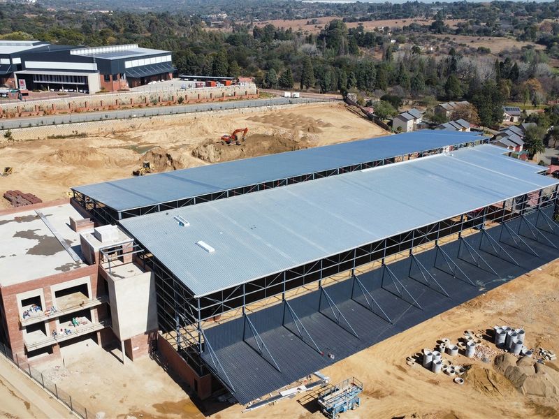 Aerial view of an industrial property under construction, featuring a large steel-framed warehouse structure with metal roofing and adjacent brick office block.