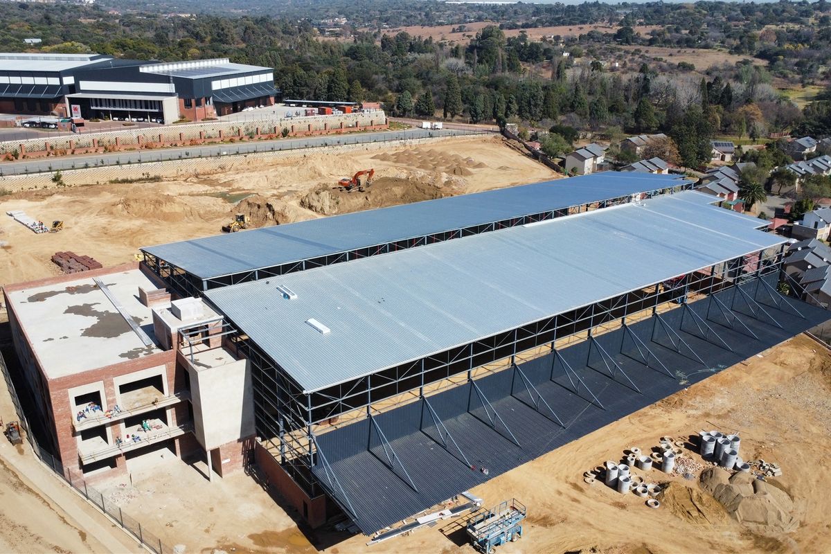 Aerial view of an industrial property under construction, featuring a large steel-framed warehouse structure with metal roofing and adjacent brick office block.