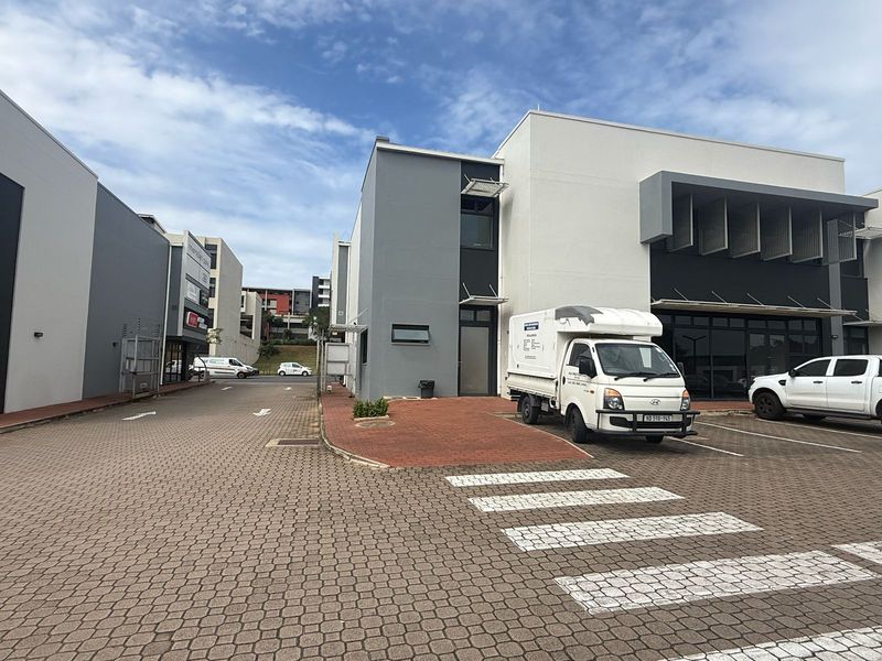 Modern commercial retail complex featuring a paved driveway, contemporary painted facade, and glass entrance doors with dedicated parking bays.
