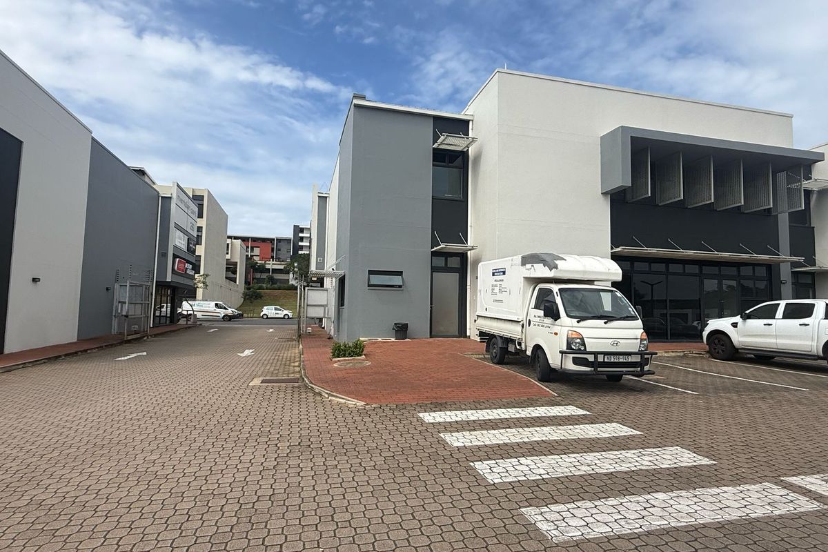 Modern commercial retail complex featuring a paved driveway, contemporary painted facade, and glass entrance doors with dedicated parking bays.